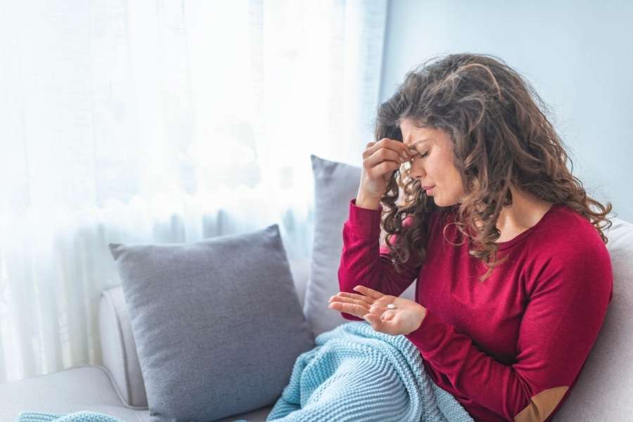 Une femme assise sur un canapé, tenant sa main sur son front et un comprimé dans l'autre, souffrant de violentes migraines ophtalmiques.