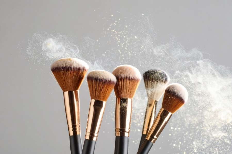 Un ensemble de pinceaux de maquillage propres avec des manches cuivrés, projetant un nuage de poudre fine.