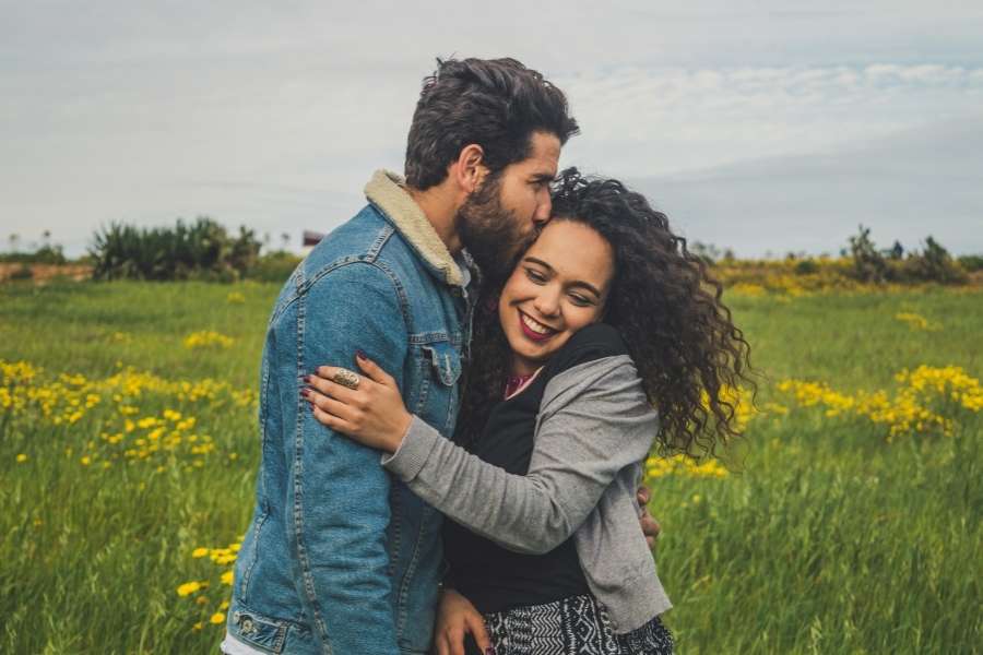 Un homme embrasse le front d'une femme qui sourit dans un champ.